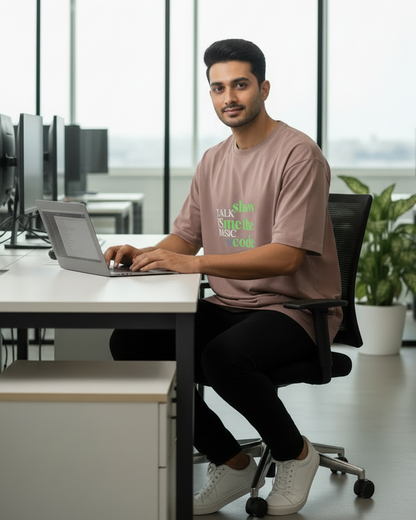 A almond color short-sleeve t-shirt with a typographic graphic on the chest reading 'show talk is the basic code' in green and white, displayed against a light gray background.