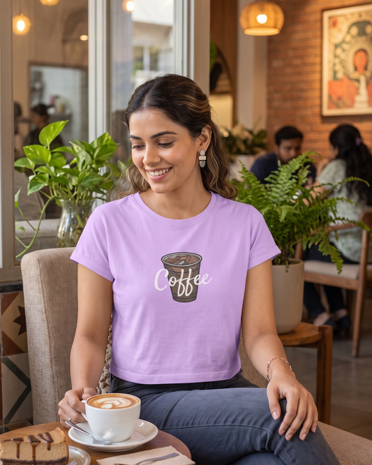 Woman wearing a lavender crop top with “Coffee” written on it, styled for coffee lovers and holding a hot cappuccino